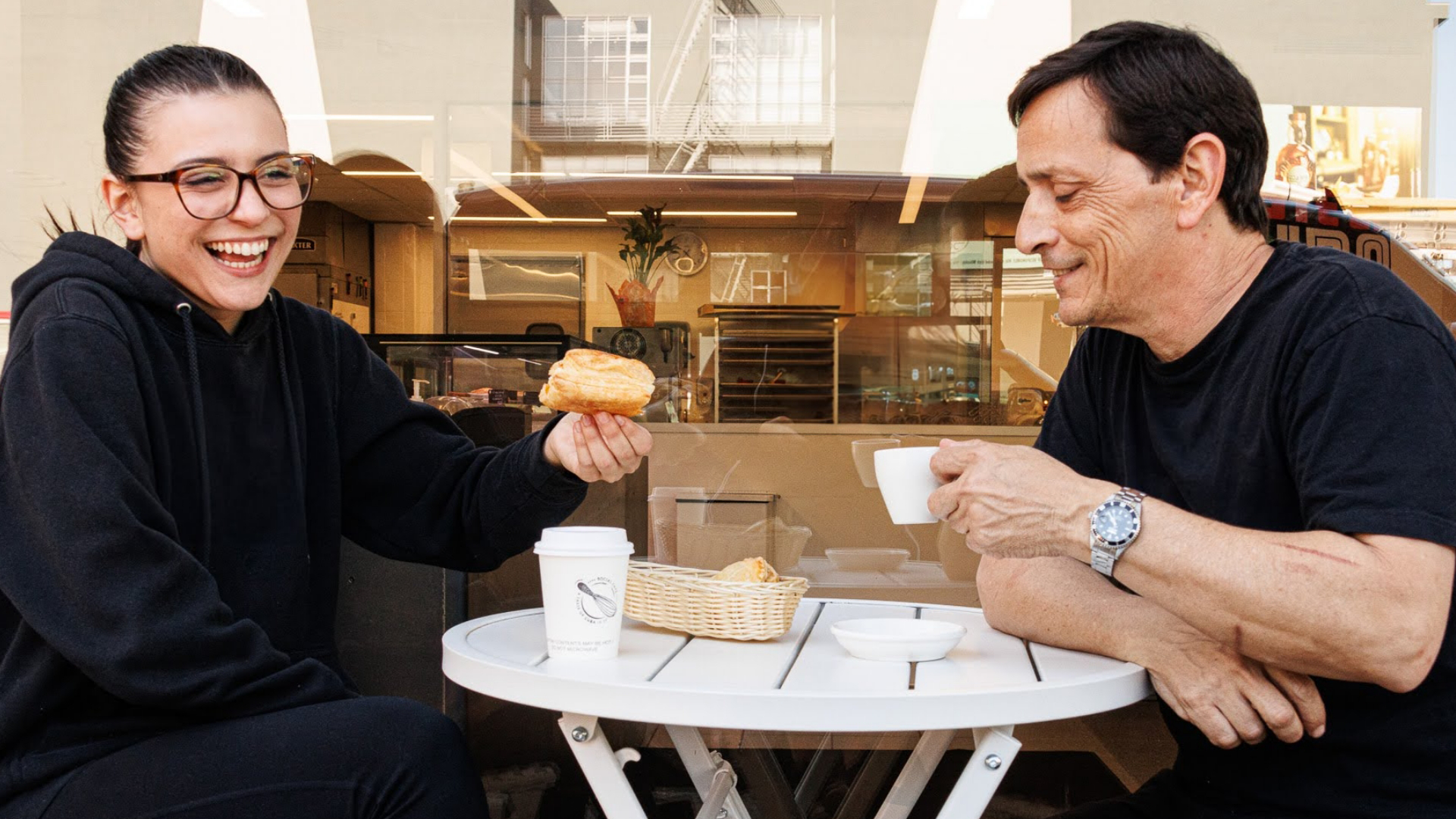 Two employees sitting outside the social cafe laughing and enjoying Cuban pastries and coffee