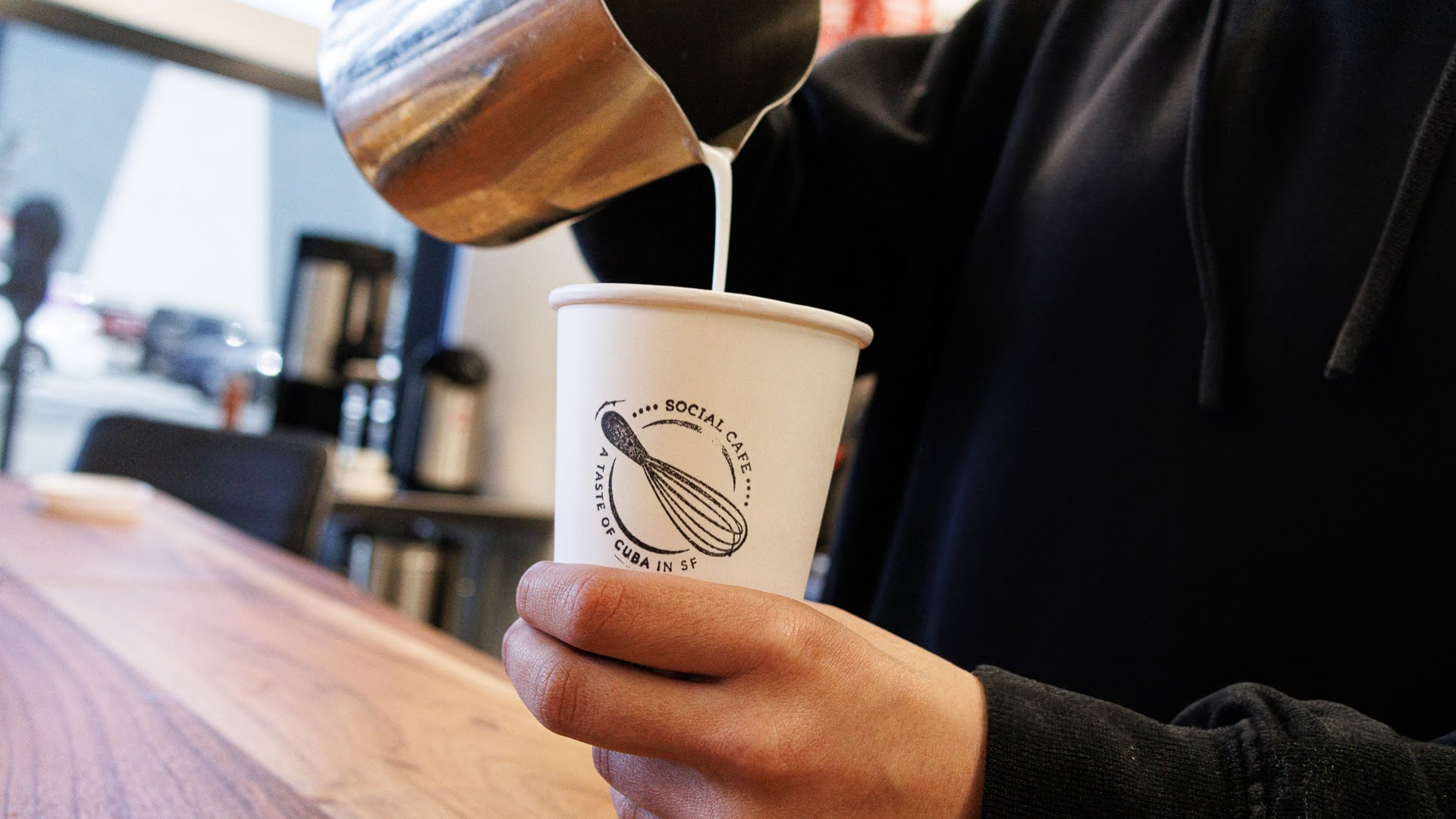Barista pouring steamed milk into to go coffee cup at Social Cafe in San Francisco