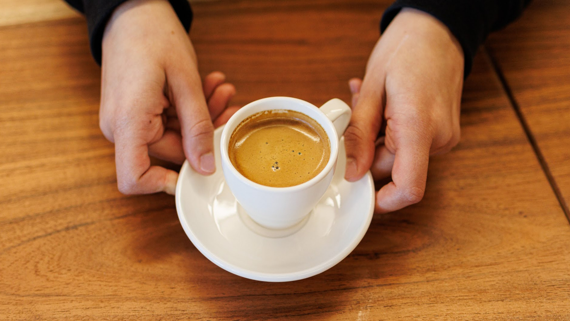 Hands holding Cuban coffee in a white mug on a wooden table
